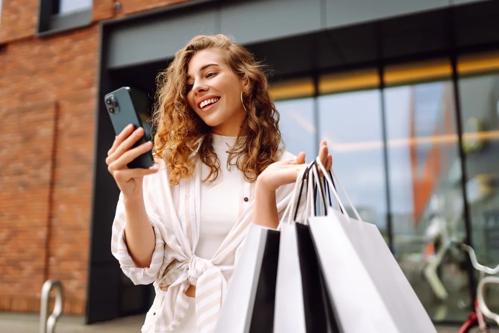 A woman holding shopping bags while on her phone.