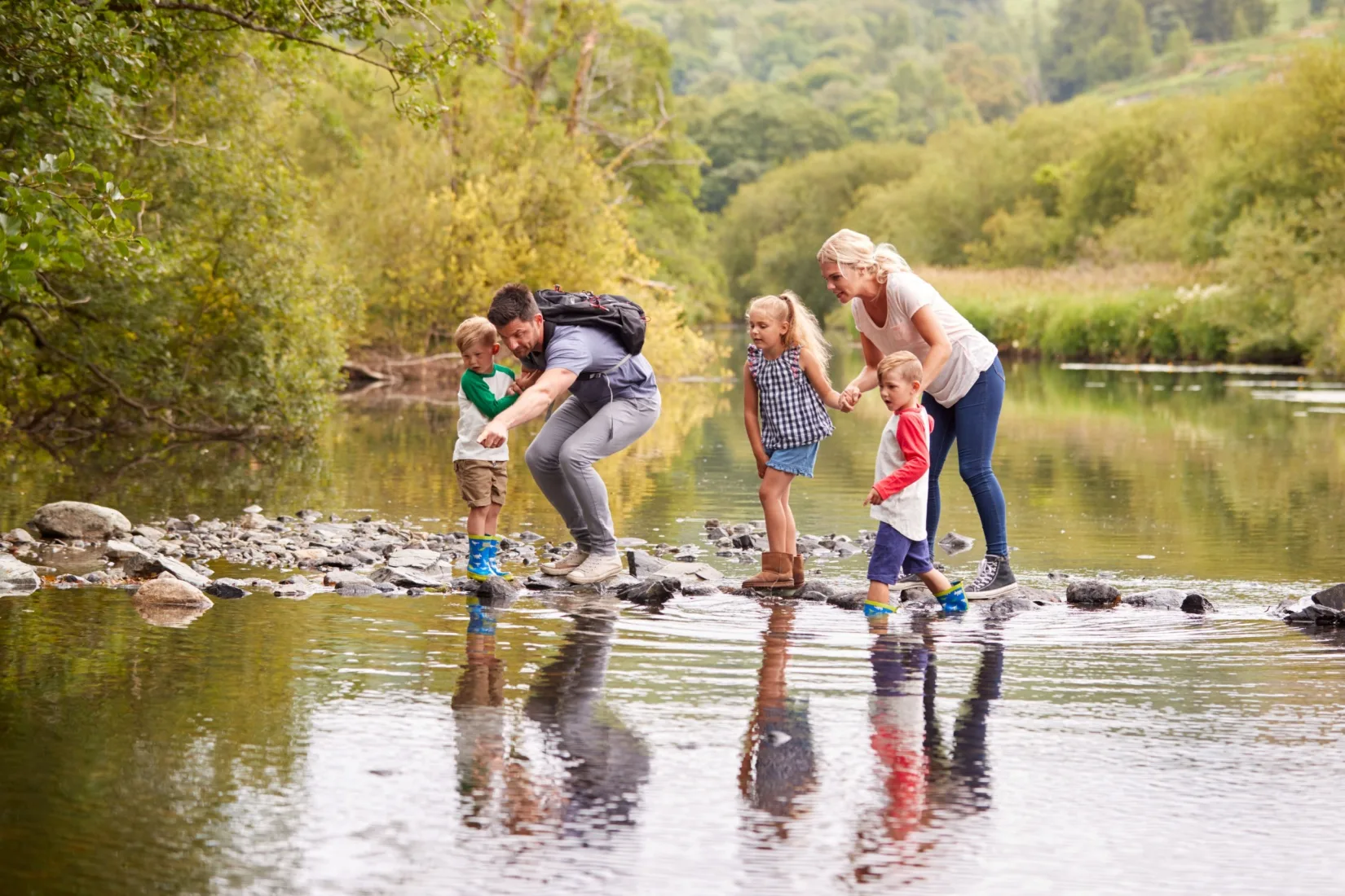 A family with young children crossing a river while hiking.