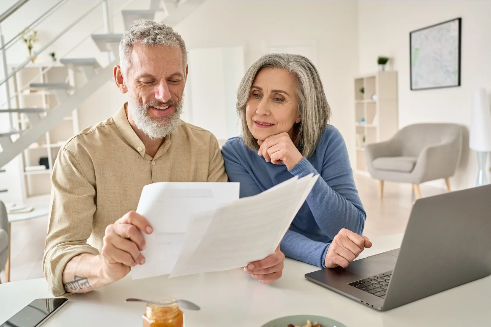 A senior couple sit at a laptop comparing multiple documents