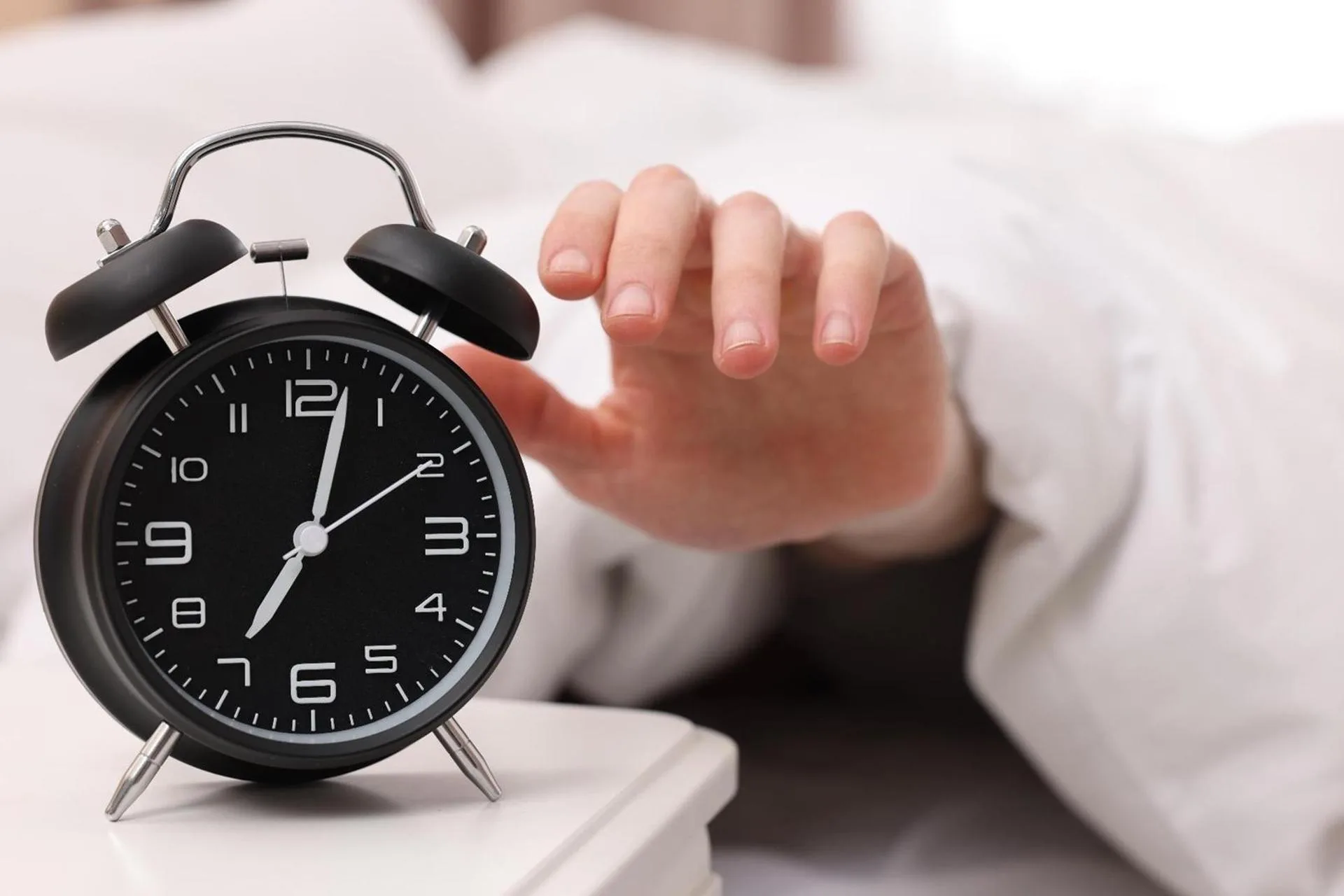 A person reaching to turn off an alarm clock.